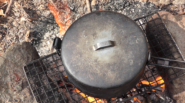 boiling a pot over a campfire with a cooking grate set on two rocks while camping in the woods